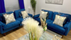 A living room with a blue sofa set, a glass coffee table, and a white decorative plant in the foreground. - Modern 3 Bed Home ,Families and Contractor Stay with Free Parking (Kingston upon Hull)