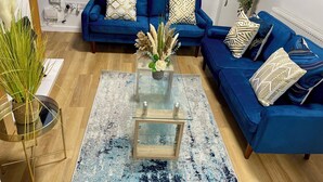 A modern living room with a blue sofa set, a glass coffee table, and decorative plants. - Modern 3 Bed Home ,Families and Contractor Stay with Free Parking (Kingston upon Hull)