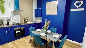 A modern kitchen with blue cabinets, a marble backsplash, and a dining area with blue chairs and a gray table. - Modern 3 Bed Home ,Families and Contractor Stay with Free Parking (Kingston upon Hull)