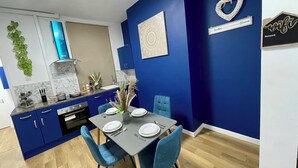 A modern kitchen with blue cabinets, a dining table set for two, and a decorative wall piece. - Modern 3 Bed Home ,Families and Contractor Stay with Free Parking (Kingston upon Hull)