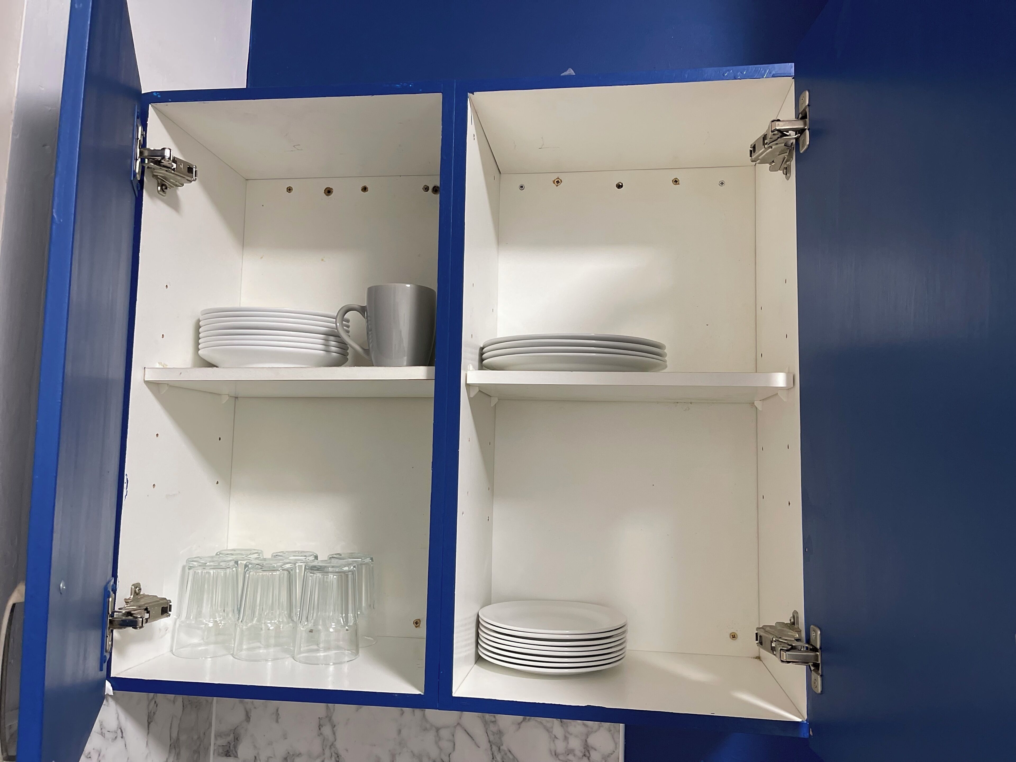 A kitchen cabinet with two shelves, each holding stacks of white plates and clear glass cups.