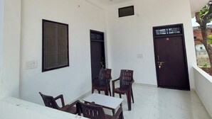 A room with a white tiled floor, a white table with four chairs, two windows with metal grills, and a black door with a lock. - Vinayak Guest House  (Faizabad)