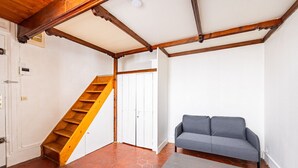 A room with a wooden staircase, a grey sofa, and a tiled floor.