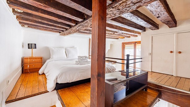 A bedroom with a wooden ceiling, a bed with white linens, a nightstand, and a lamp.