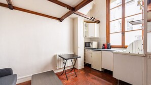 A compact kitchen with white cabinets, a small table, and a window with a view of buildings.