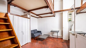 A compact living space with a wooden staircase, a grey sofa, a small table, and a radiator.