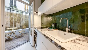 Een moderne keuken met een grote witte spoelbak, een groene betegelde achterwand, en uitzicht op een bamboomscherm.