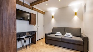 Een moderne kamer met een bank, twee stoelen, een televisie en een houten vloer.