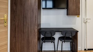 Een kamer met een houten garderobe, een bureau met twee stoelen, een wandtelevisie, en zichtbare houten balken aan het plafond.