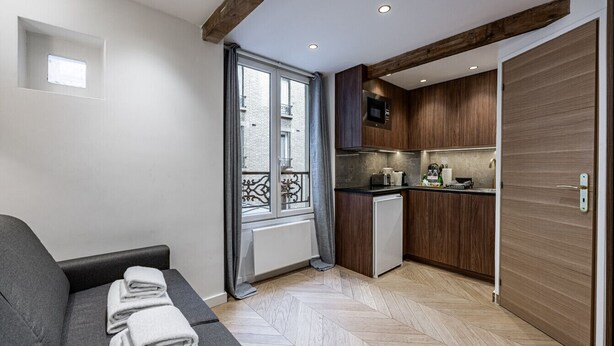 Een compact woongedeelte met een bank, een kleine kitchenette en uitzicht op buiten door een raam.