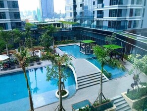 Une piscine intérieure moderne à plusieurs niveaux, entourée de palmiers et de verdure, et offrant une vue sur le paysage urbain.