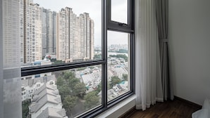 A room with a large window overlooking a cityscape, including high-rise buildings and residential areas. - OPAL SAIGON PEARL Premier Residence (Ho Chi Minh City)