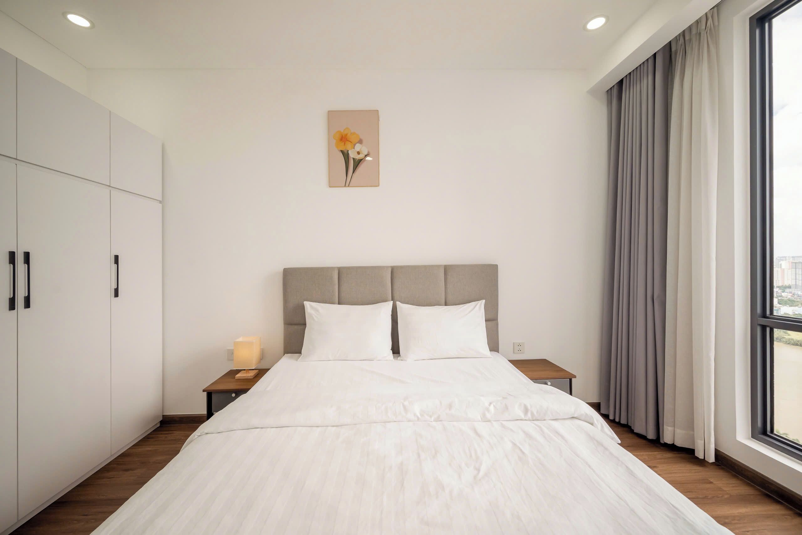 A modern bedroom with a large bed, a nightstand, a wall-mounted artwork, and a window with curtains.