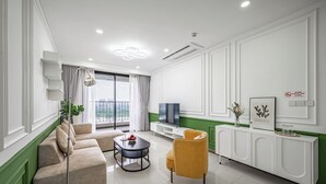 A modern living room with a sofa, coffee table, and armchair, a flat-screen TV, and a green accent wall. - OPAL SAIGON PEARL Premier Residence (Ho Chi Minh City)