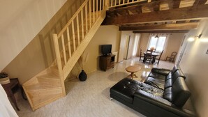 A spacious living area with a wooden staircase, a black leather sofa, a wooden coffee table, and a television. - L'Étoile Normande - Country house (Bourgnac)