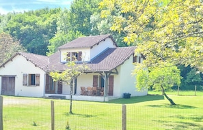 Une maison à deux étages, avec un toit en tuiles, une véranda avec des chaises et une cour clôturée.