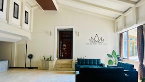 A spacious lobby with a high ceiling, a central staircase, and a seating area with sofas. A wall-mounted sign reads "THE ROYALTY OF GOA". - The Regalia Goa (Alto de Porvorim)