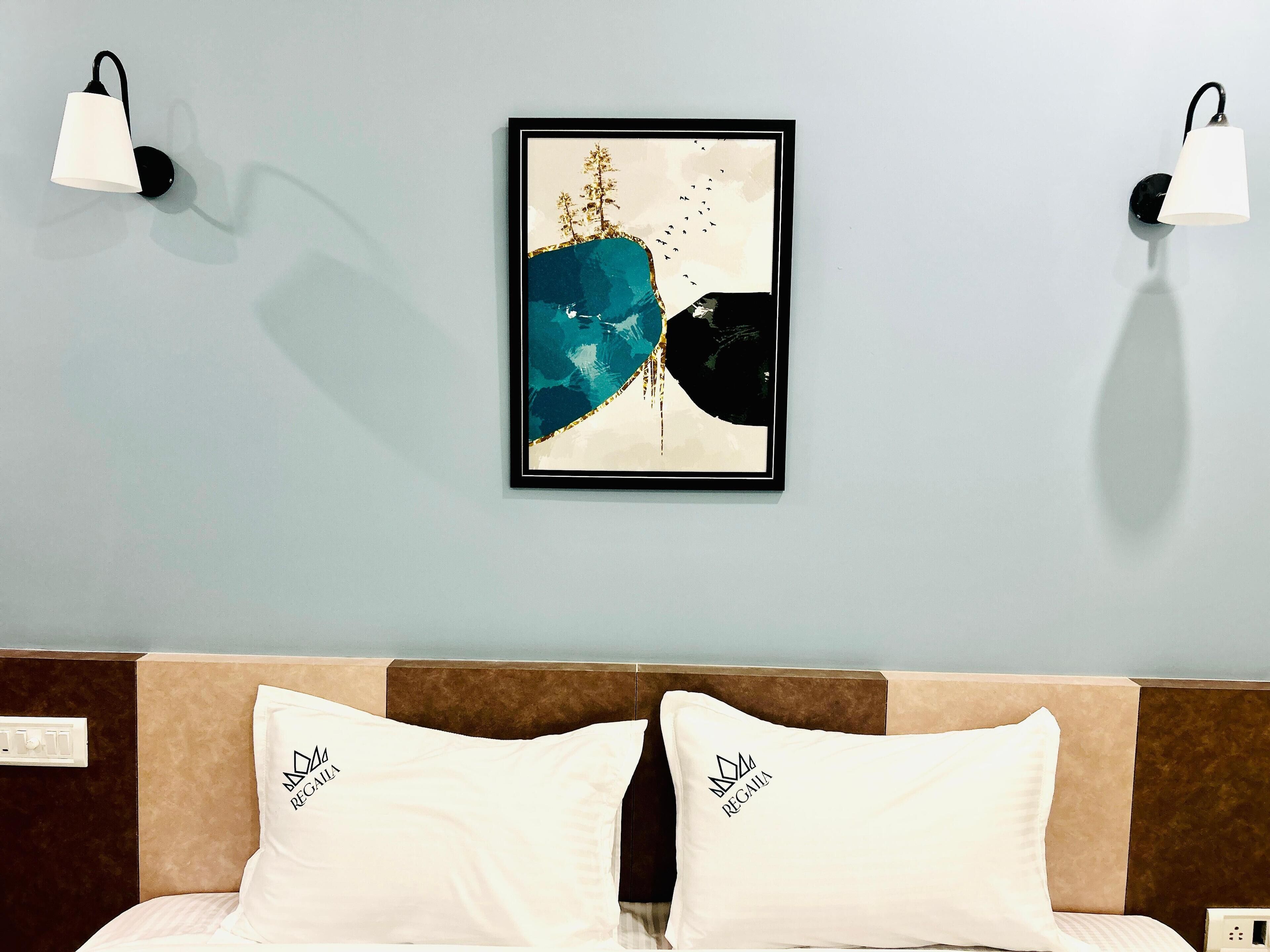 Una habitación de hotel con una cama, dos lámparas adosadas a la pared y un cuadro abstracto enmarcado.