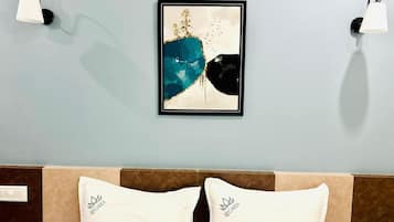 A hotel room with a bed, two wall-mounted lamps, and a framed abstract painting.
