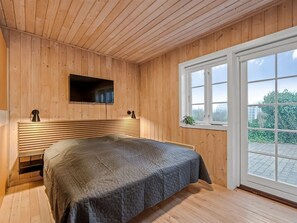 Relax in this serene bedroom with a large bed and flat-screen TV, offering a peaceful view of the surrounding greenery.