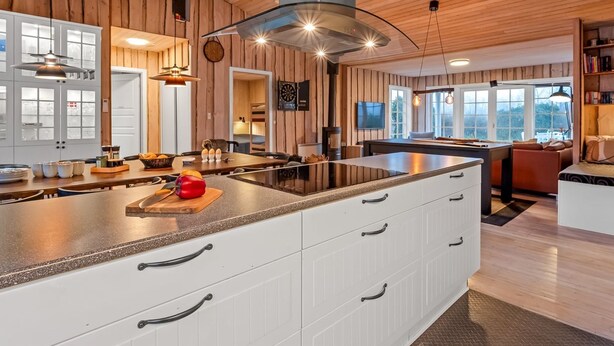 A modern kitchen with a central island, wooden panel walls, and a large window providing natural light.