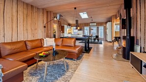 A cozy wooden interior with a leather sofa, a dining area, and a wood-burning stove.