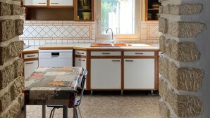 Een keuken met stenen muren, houten kastjes, een raam en een tafel met stoelen.