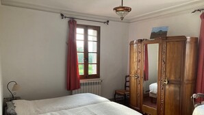 Een slaapkamer met een groot bed, een houten garderobe, een radiator, een raam met gordijnen en een lamp.
