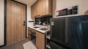 A modern kitchen with wooden cabinets, a stainless steel sink, a black refrigerator, and a microwave. - DE LA SOL Premier Residence (Ho Chi Minh City)