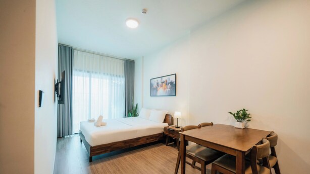 A hotel room with a bed, bedside table, lamp, and a dining table with chairs. - DE LA SOL Premier Residence (Ho Chi Minh City)