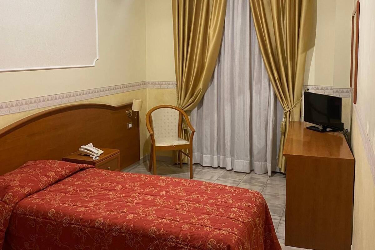 Una habitación de hotel con cama, una silla, un escritorio y televisor, además de cortinas.