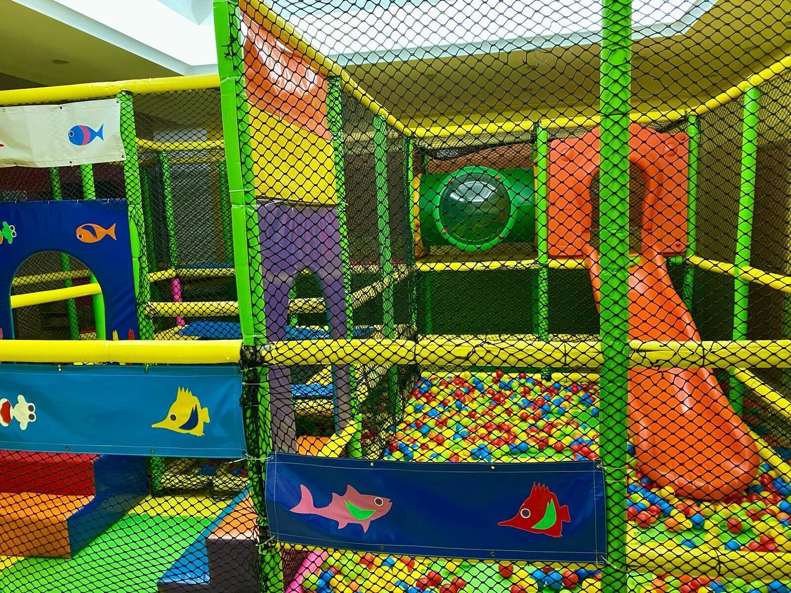 A multi-level indoor play area with various play structures, including slides and climbing areas, enclosed by safety netting.