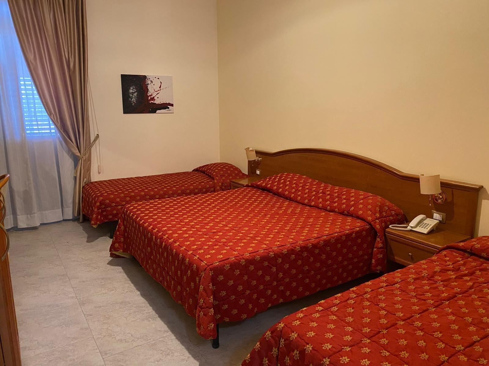 A hotel room with two beds, a bedside table with a lamp, and a painting on the wall.