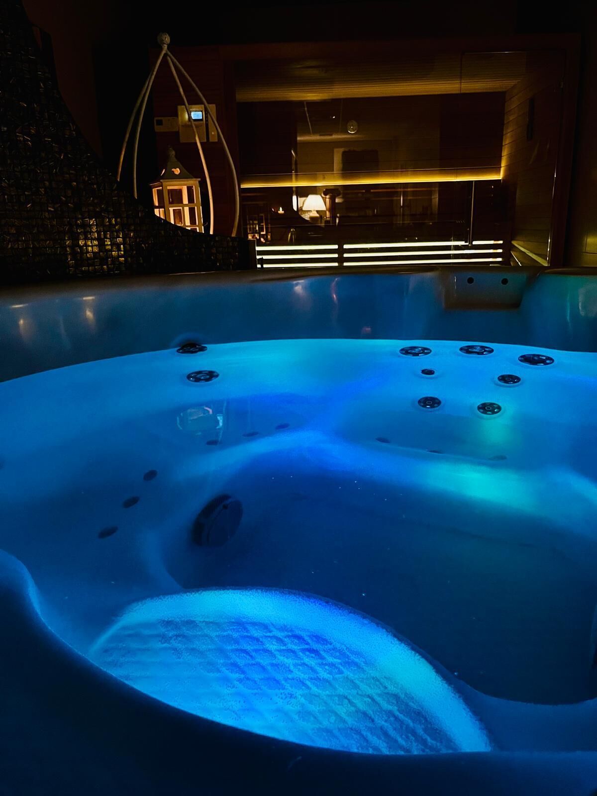 A hot tub with jets, surrounded by a modern interior with a visible pool and a unique architectural feature.