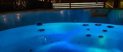 A hot tub with jets, surrounded by a modern interior with a visible pool and a unique architectural feature.