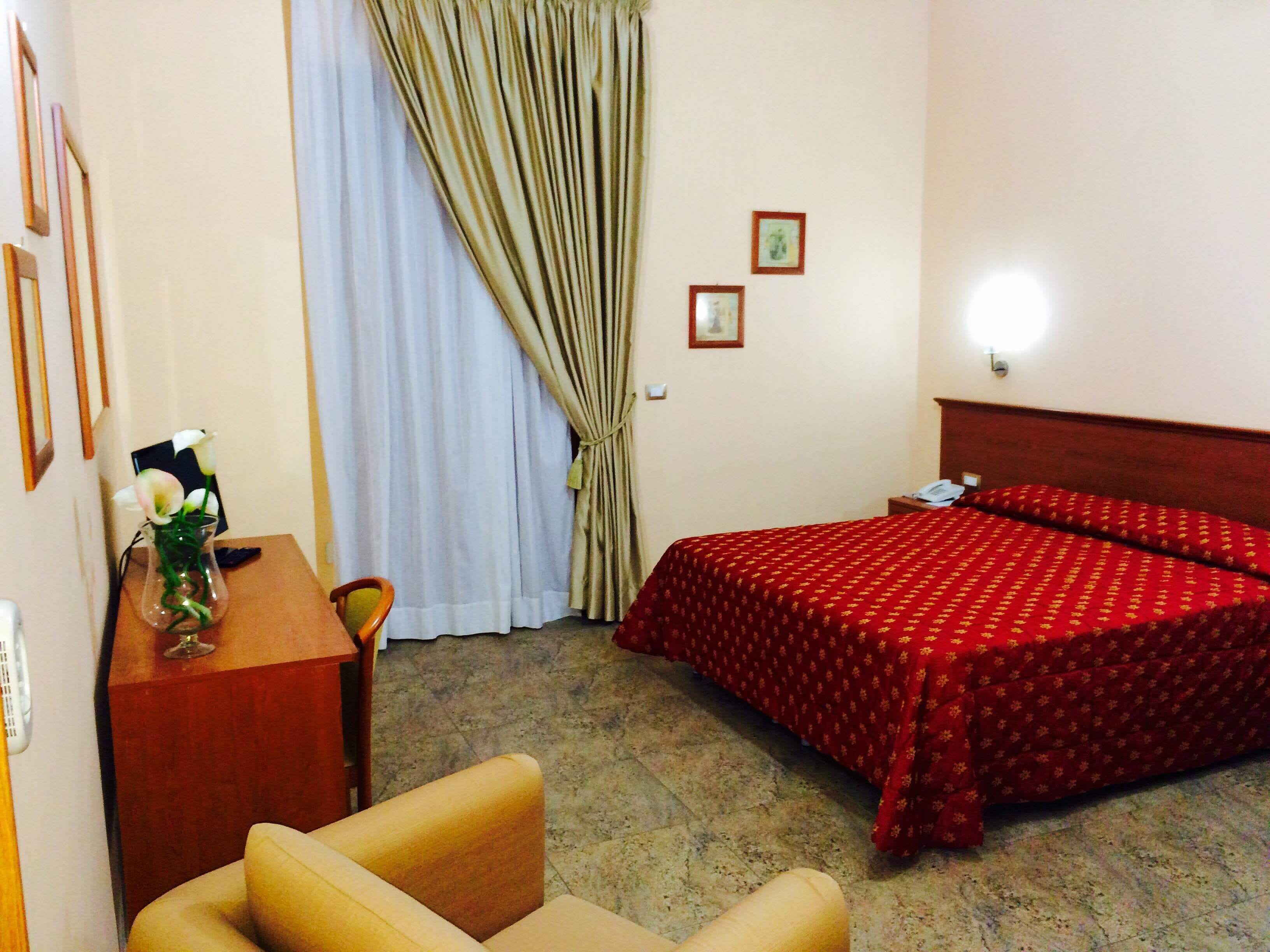A hotel room with a bed, a desk, a chair, and a vase with flowers.