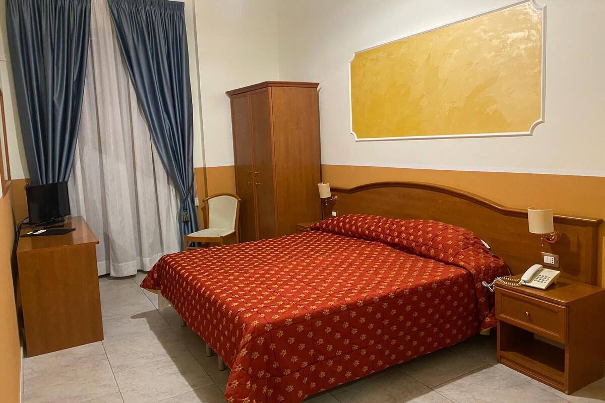 Una habitación de hotel con cama, escritorio, silla, armario y teléfono.