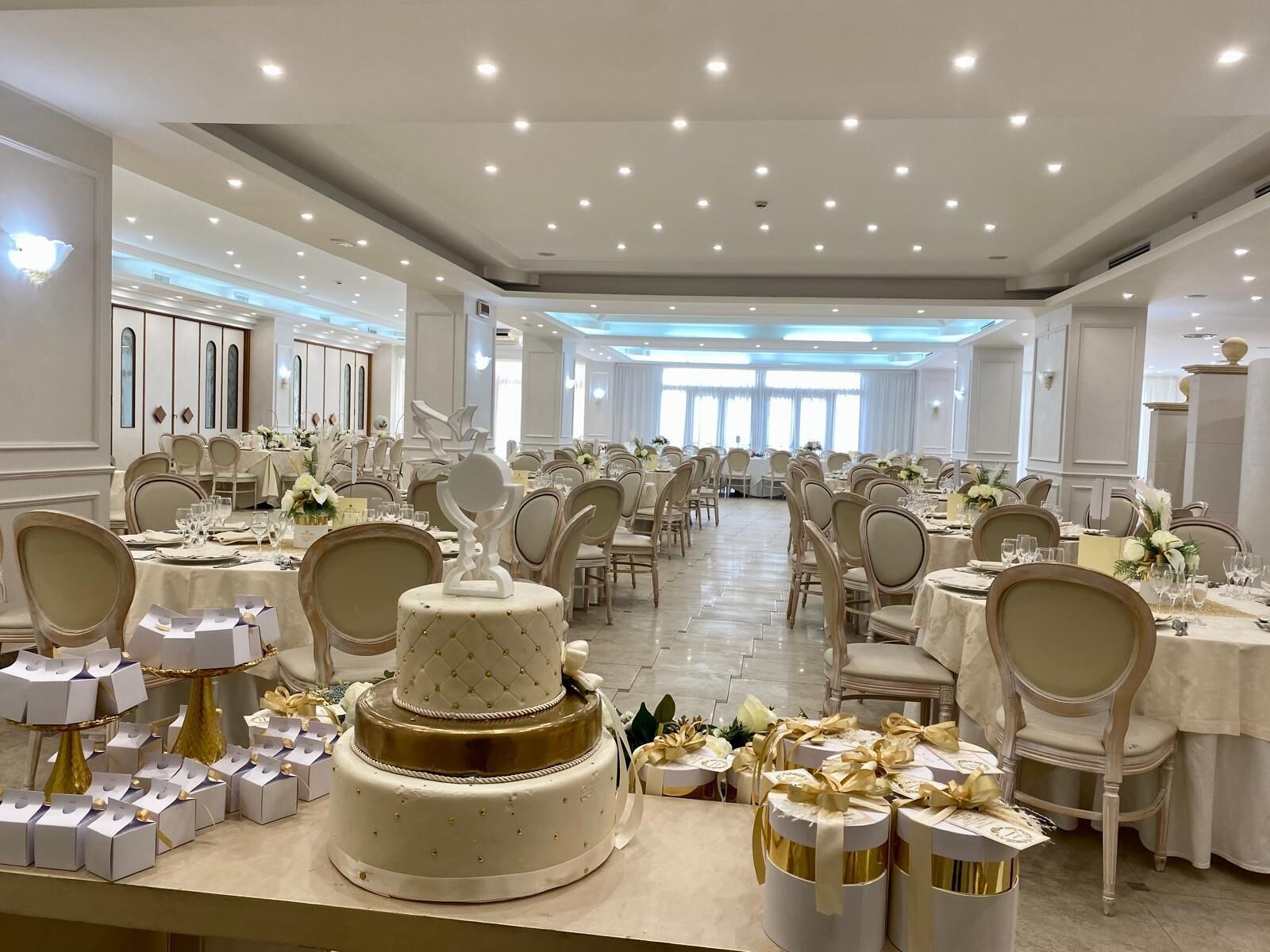 Ein Festsaal mit runden Tischen, Stühlen und einer großen mehrstöckigen Torte.