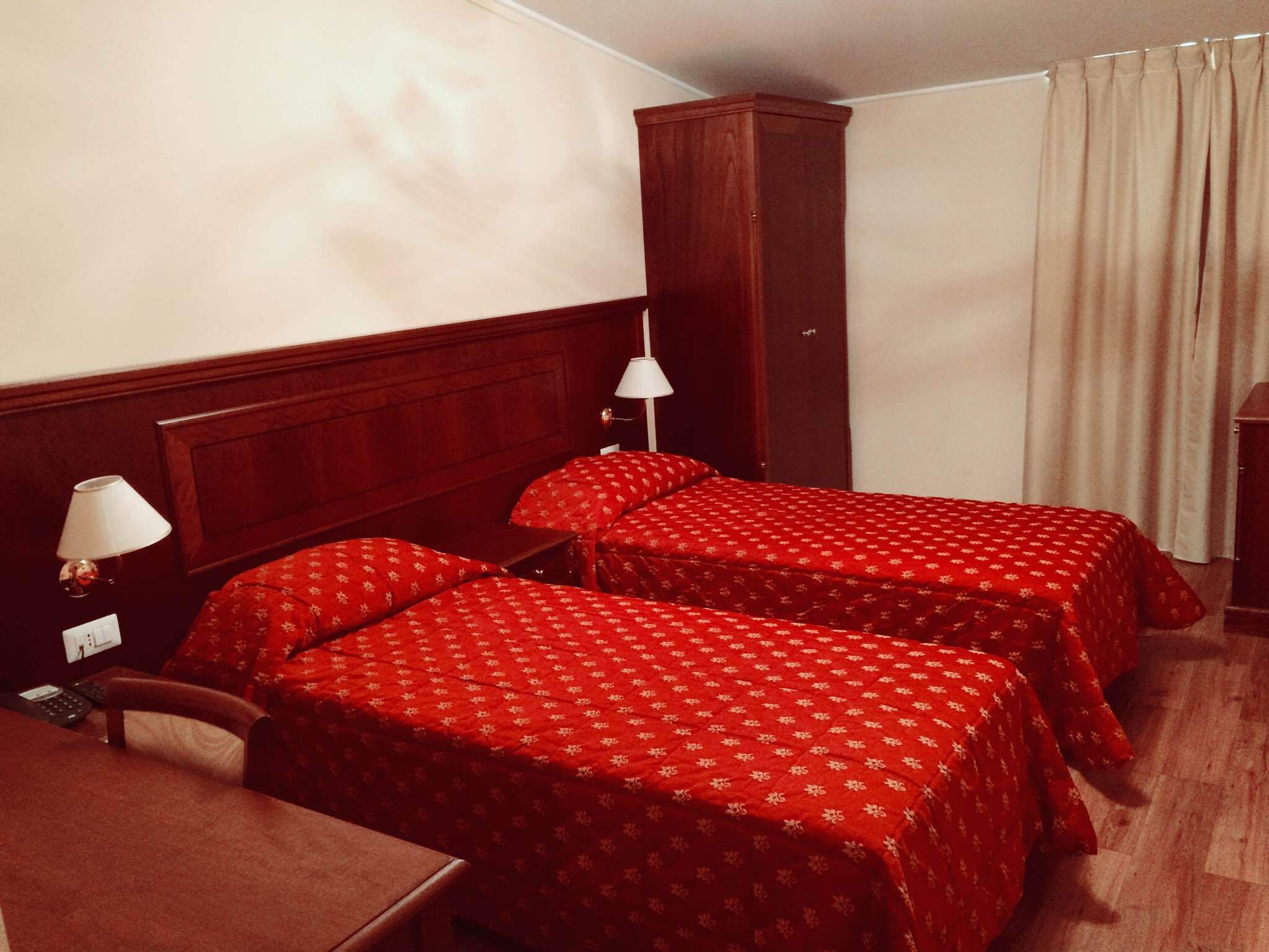 Una habitación de hotel con dos camas individuales, una mesita de noche de madera, un escritorio y un armario.