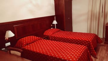 Una habitación de hotel con dos camas individuales, una mesita de noche de madera, un escritorio y un armario.