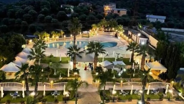 A resort with a large swimming pool, palm trees, and a view of the mountains.