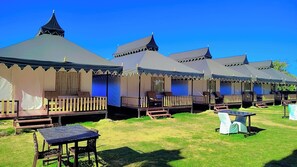 A row of tents with a covered porch and a table in the foreground. - Braham Vatika Resort (Pushkar)