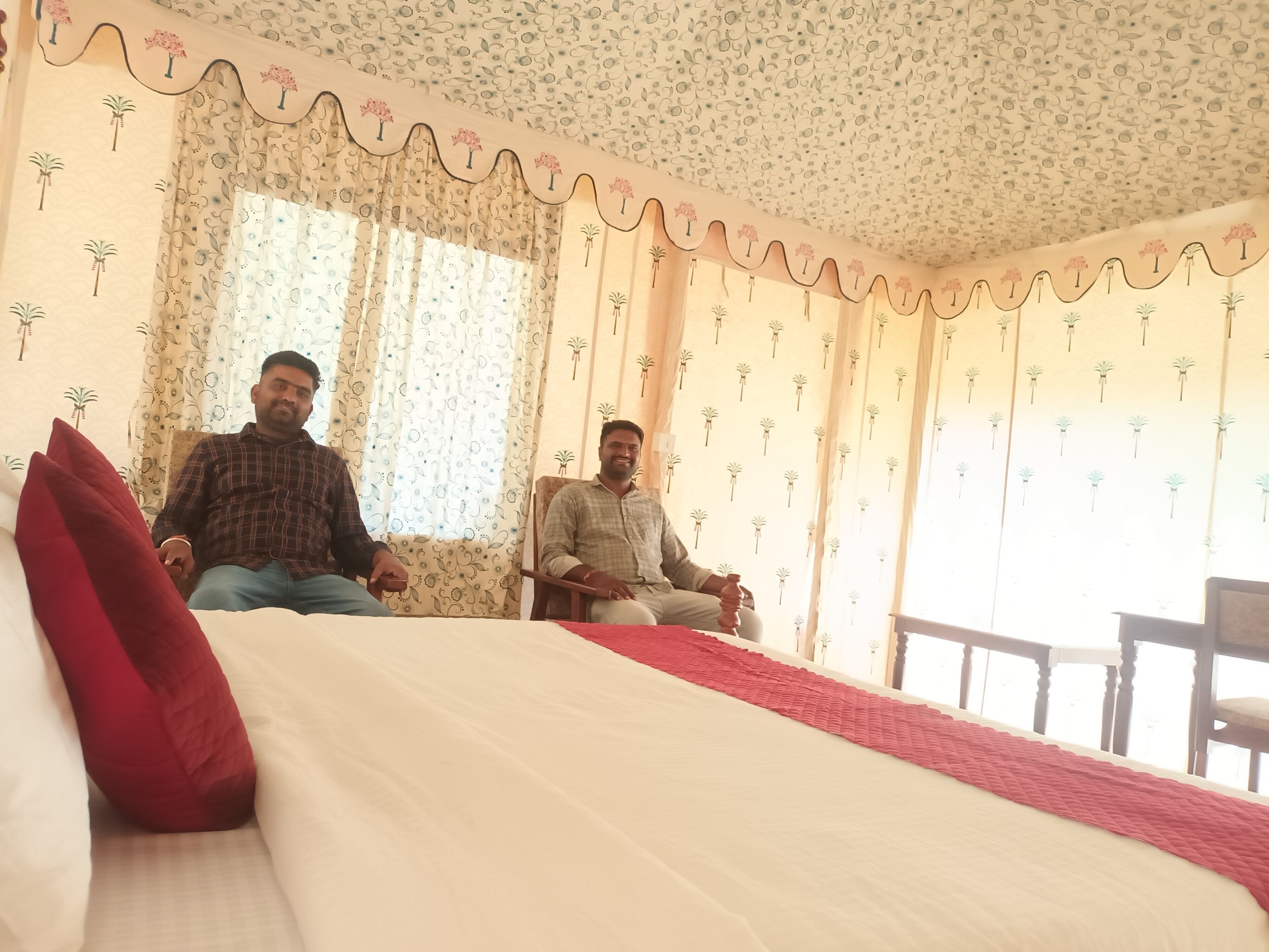 Una habitación con dos camas, papel tapiz estampado con motivos florales y una almohada roja decorativa.