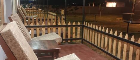 Un área de estar al aire libre cubierta con sillas y mesas de madera, una cerca y vistas al cielo nocturno.
