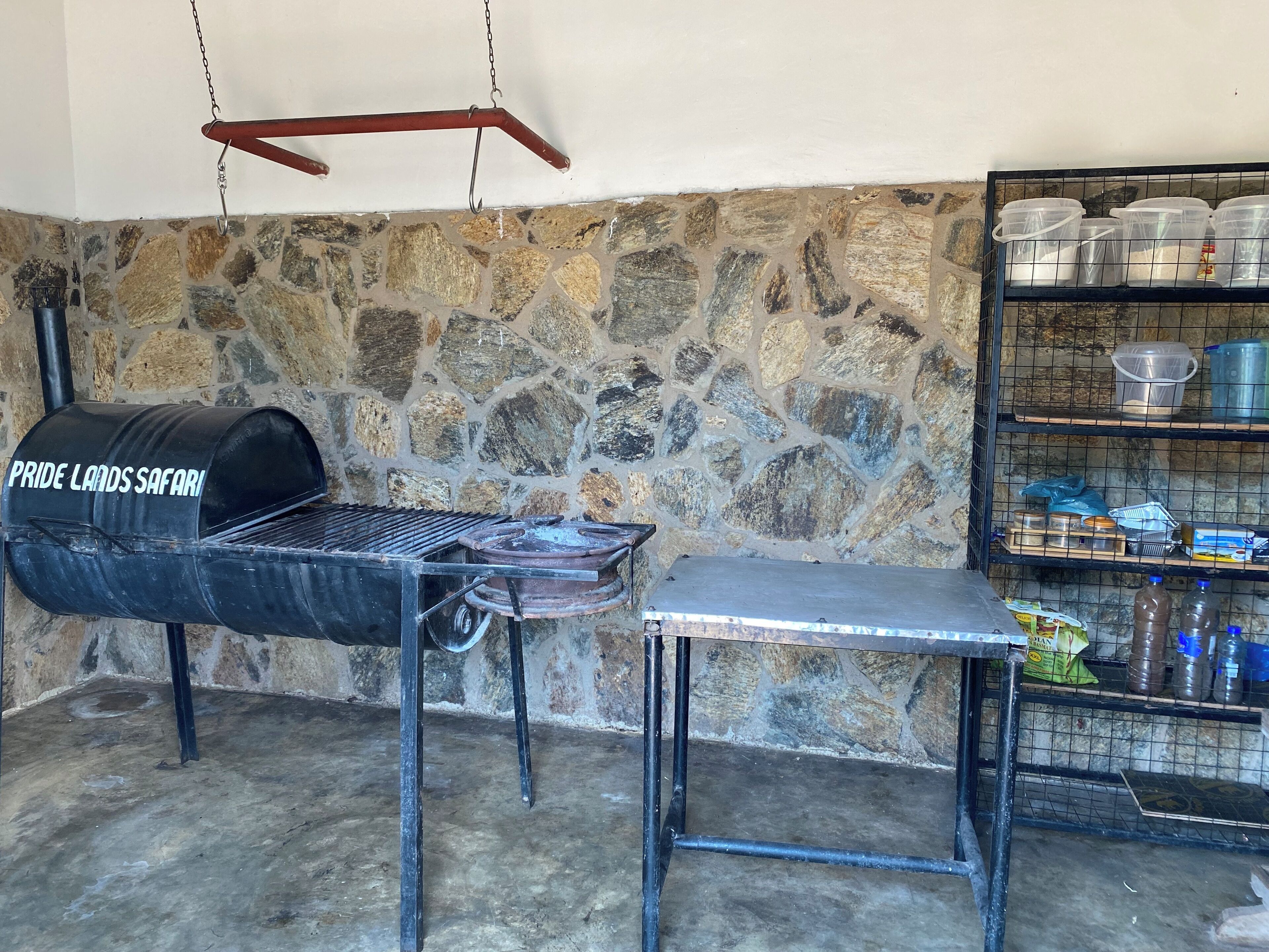 A stone wall, a charcoal grill, a metal table, and a shelf with containers.