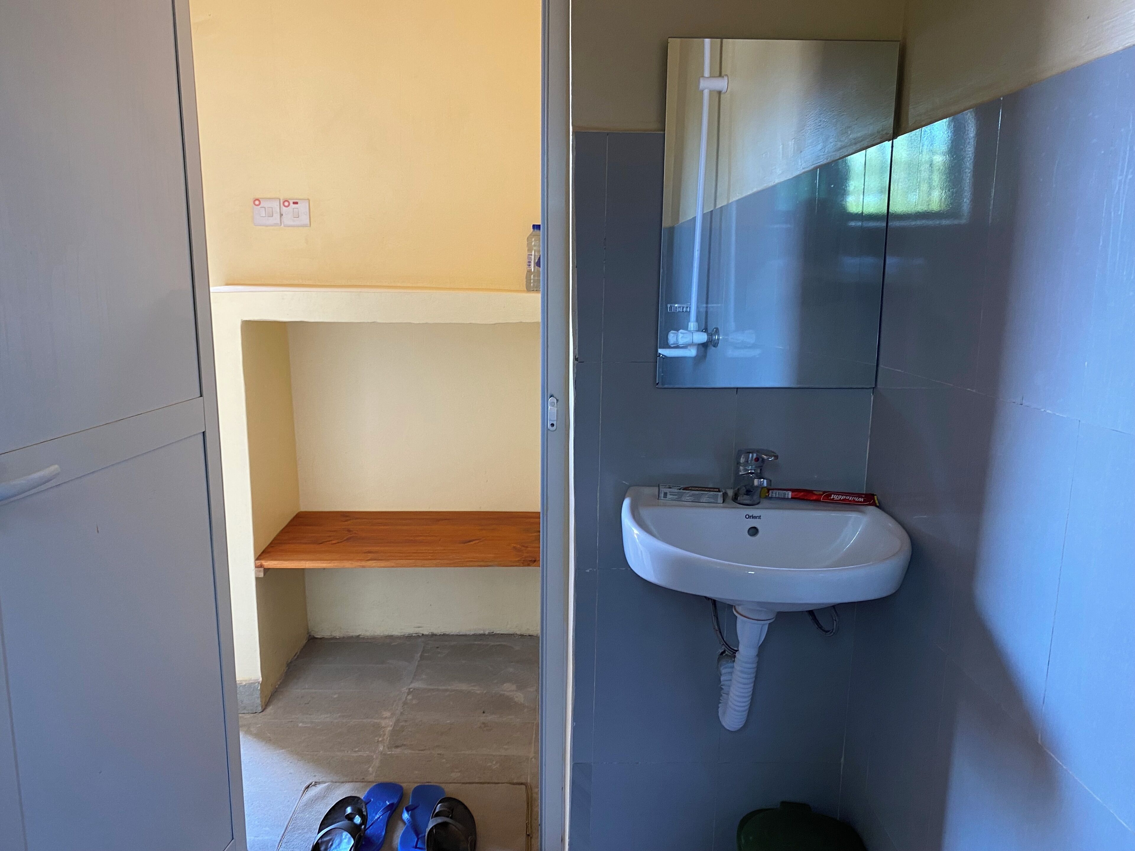 Une petite salle de bain avec un lavabo blanc, un miroir et une étagère en bois.