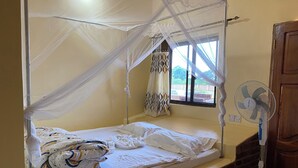 A single bed with a mosquito net, a bedside fan, and a window with curtains. - Pride Lands Safari (Morogoro)