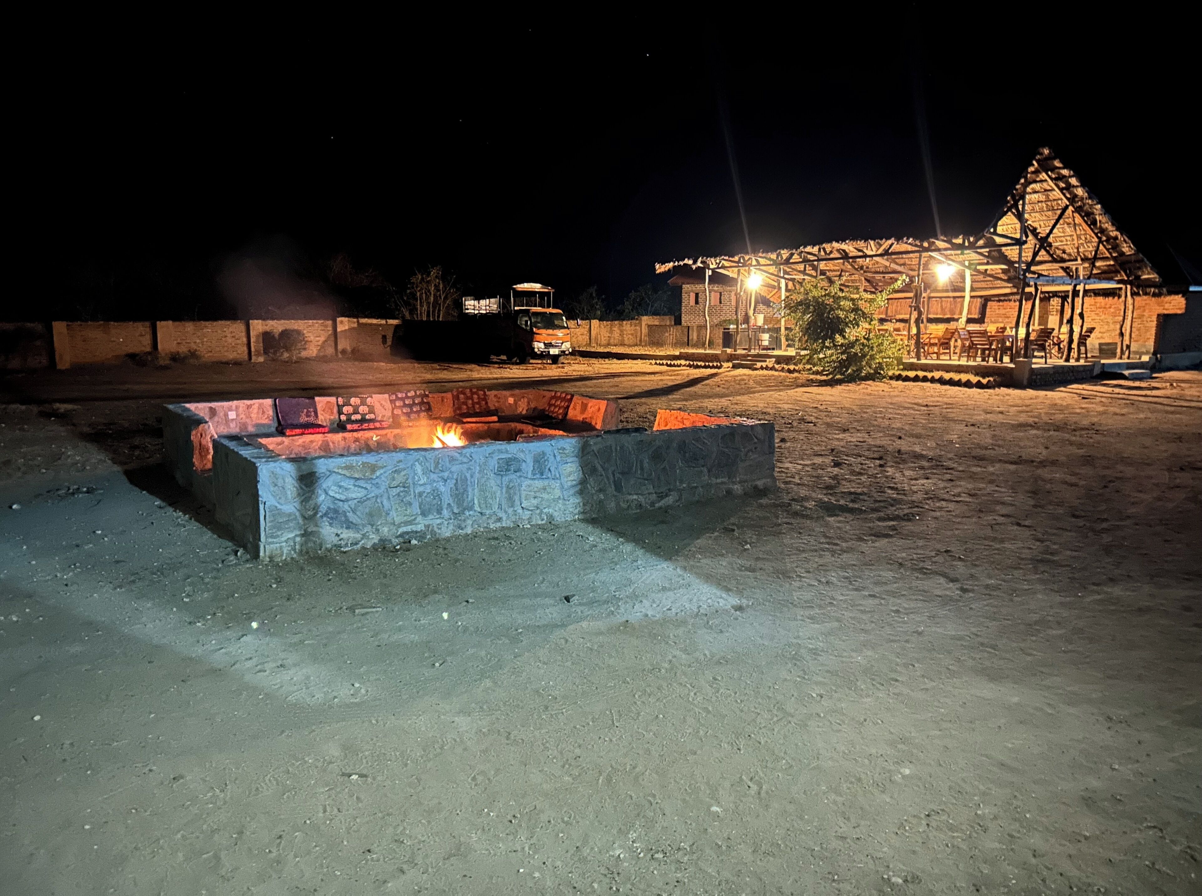 A fire pit in a sandy area with a building in the background.