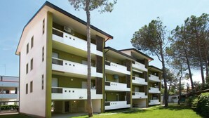 A multi-story residential building with balconies, a flat roof, and a small garden area. - Welcoming flat for a comfortable stay in Bibione (Bibione Pineda)