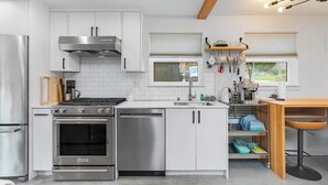 A modern kitchen with white cabinets, stainless steel appliances, and a wooden ceiling. - Ember & Glow Loft Retreat (Seattle)